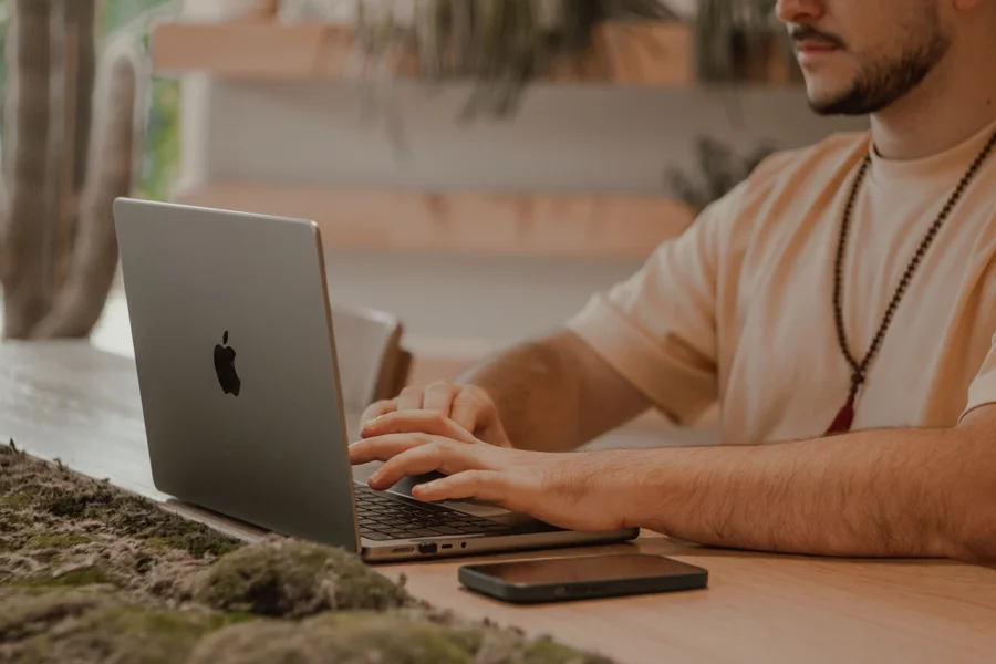 A man typing on a laptop at a sunlit desk, focused on his work, no one else around